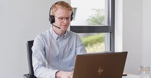 Junger, hellhäutiger Supportmitarbeiter mit Headset am Laptop